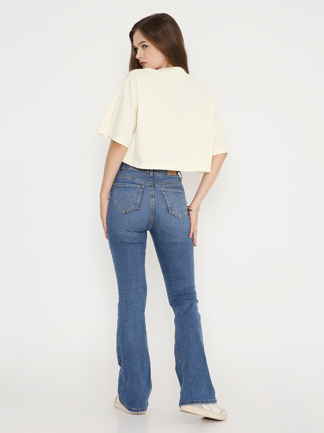 Off-white oversized crop top with short sleeves paired with blue flared jeans.