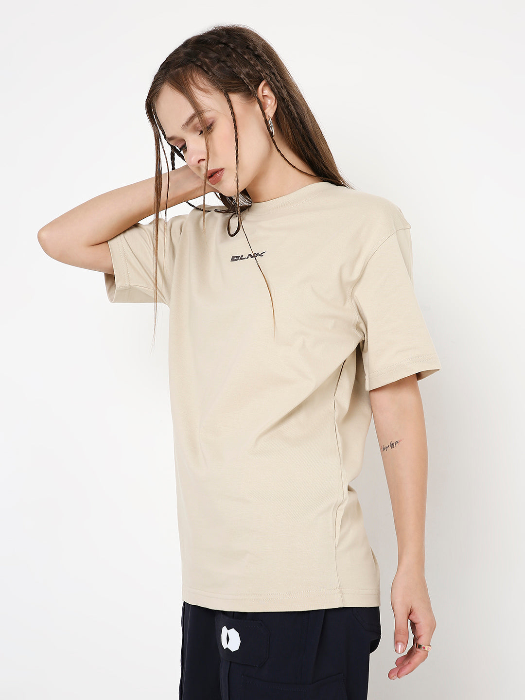Beige relaxed fit T-shirt with small black graphic detail on chest, worn with black pants.