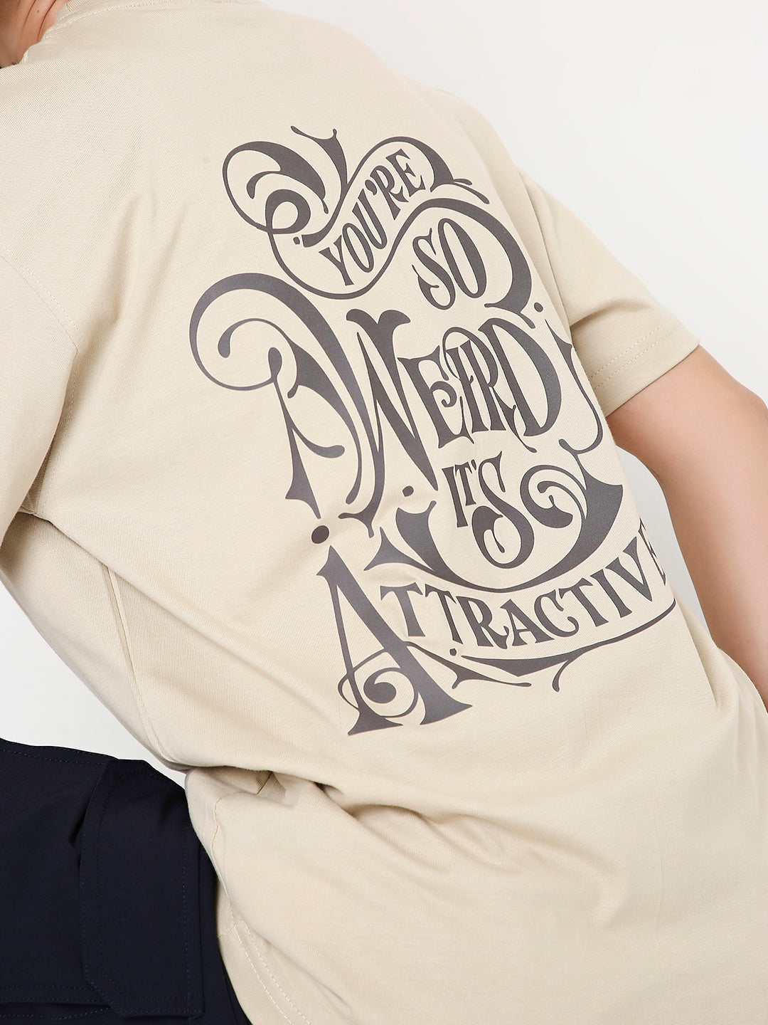 Beige relaxed fit t-shirt with large black stylized graphic text reading "You're so weird it's attractive" on the back.