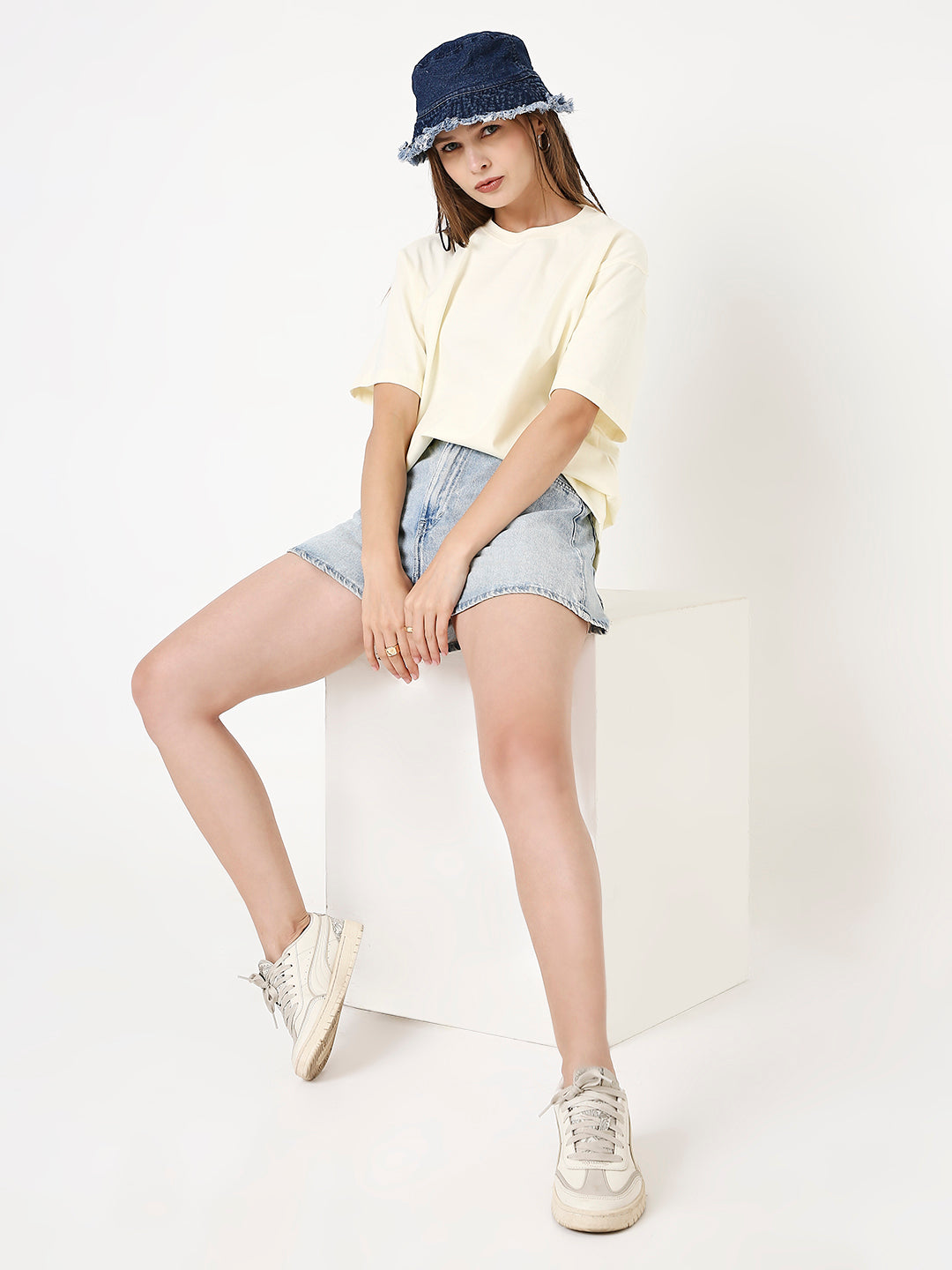 Off-white relaxed fit t-shirt paired with light denim shorts and white sneakers, blue bucket hat accessory.