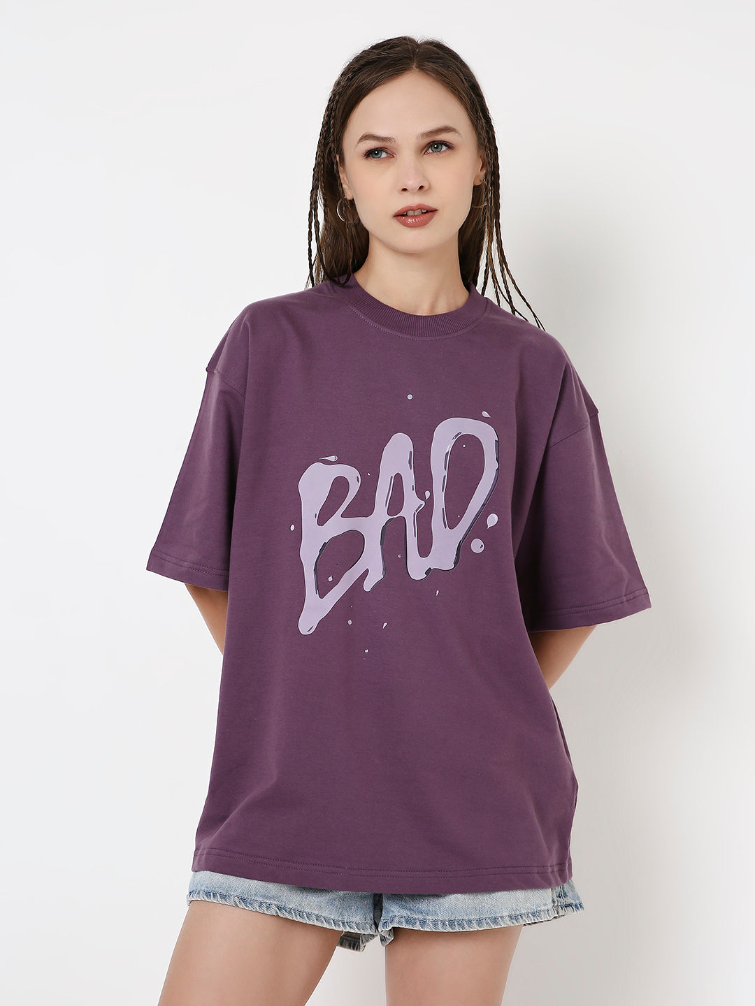Oversized grape purple t-shirt with large abstract "BAD?" text on front, worn with denim shorts.