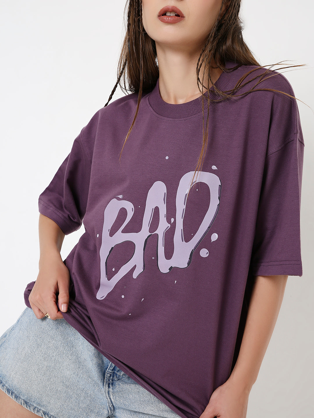 Purple oversized t-shirt with white "BAD" graffiti-style print, worn with light denim shorts.