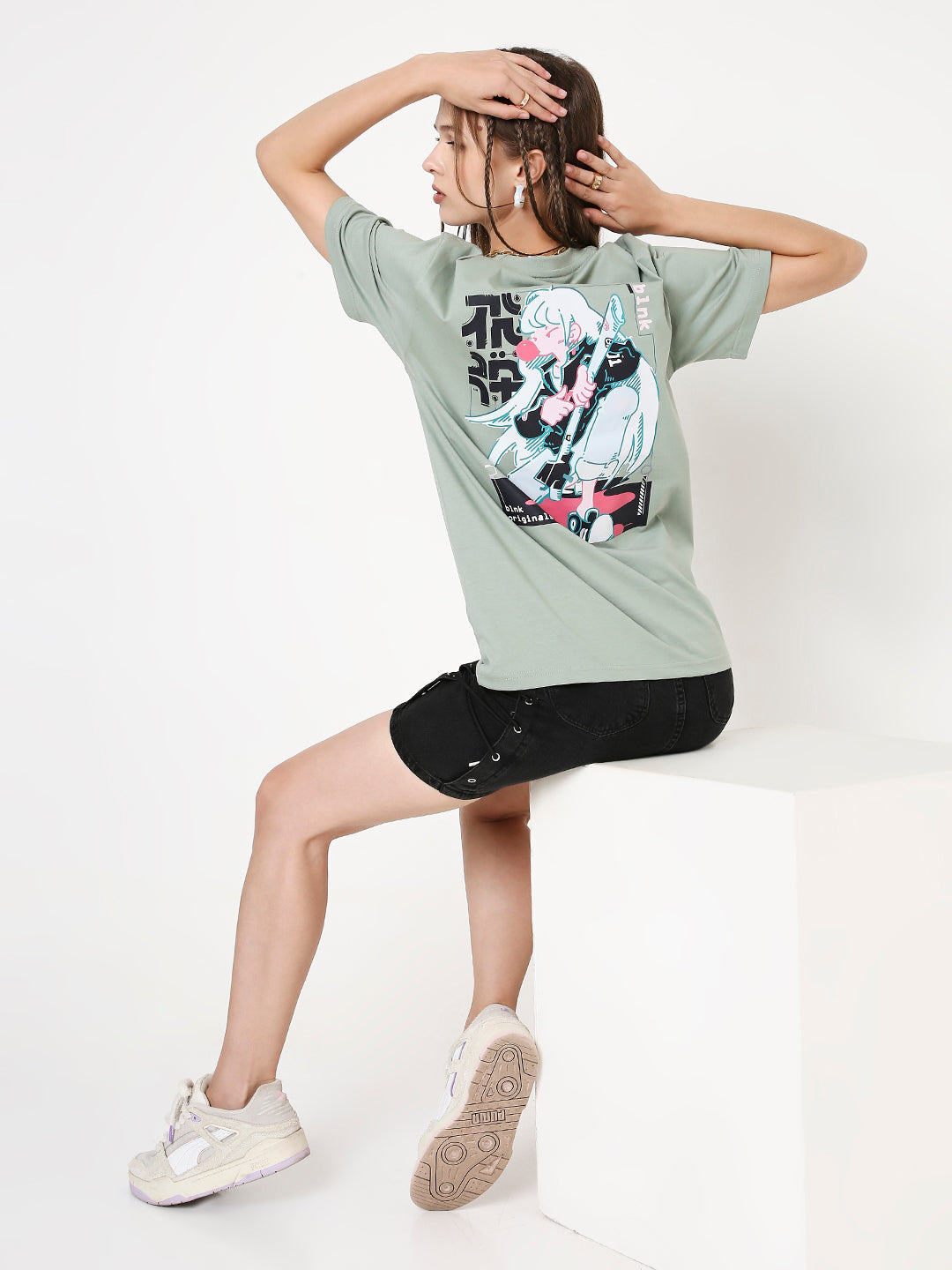 Relaxed fit sage green t-shirt with black and white graphic print, paired with black shorts and white sneakers.