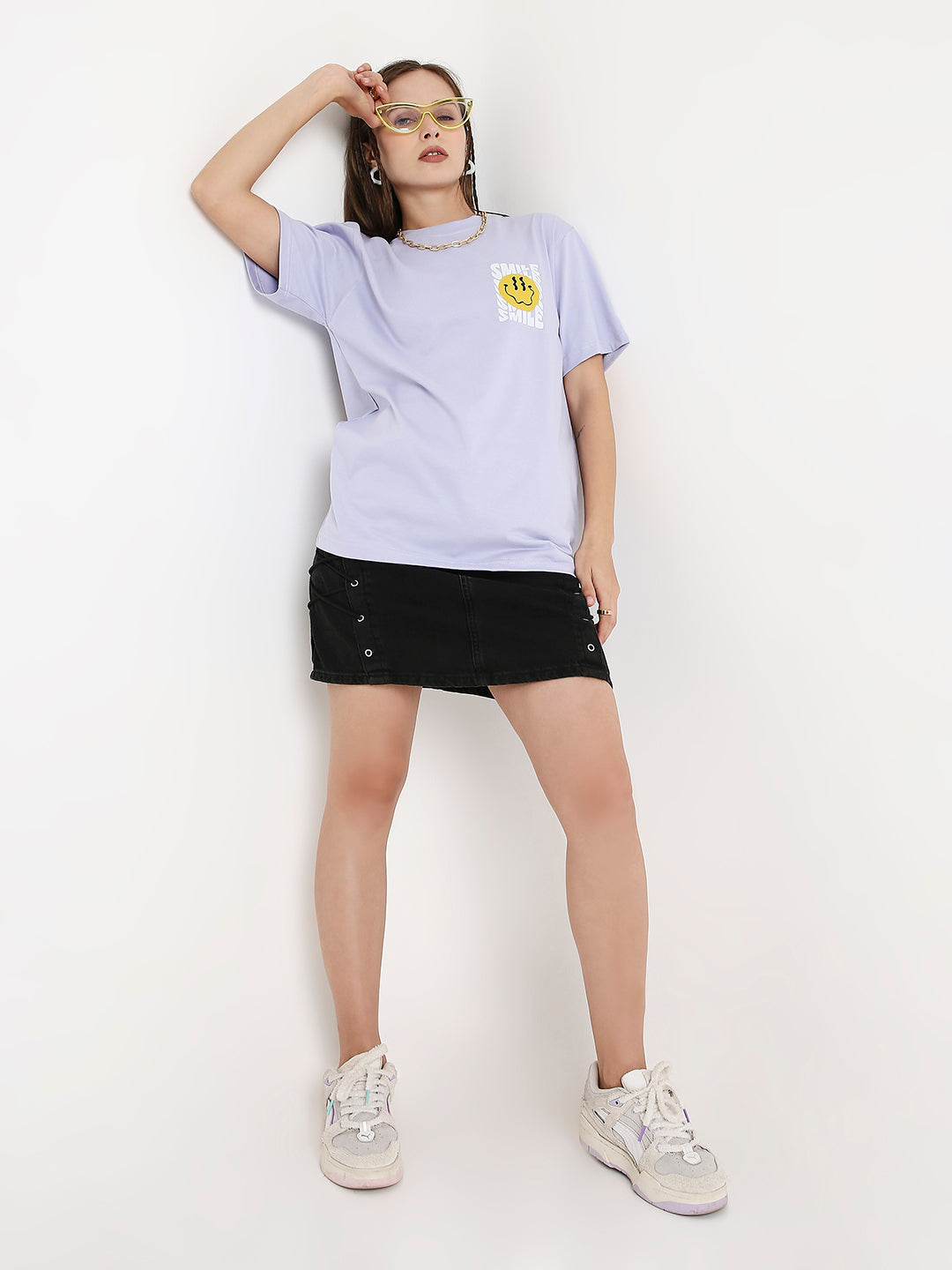 Lavender relaxed fit t-shirt with small yellow smiley face print on chest, paired with black denim mini skirt and white.