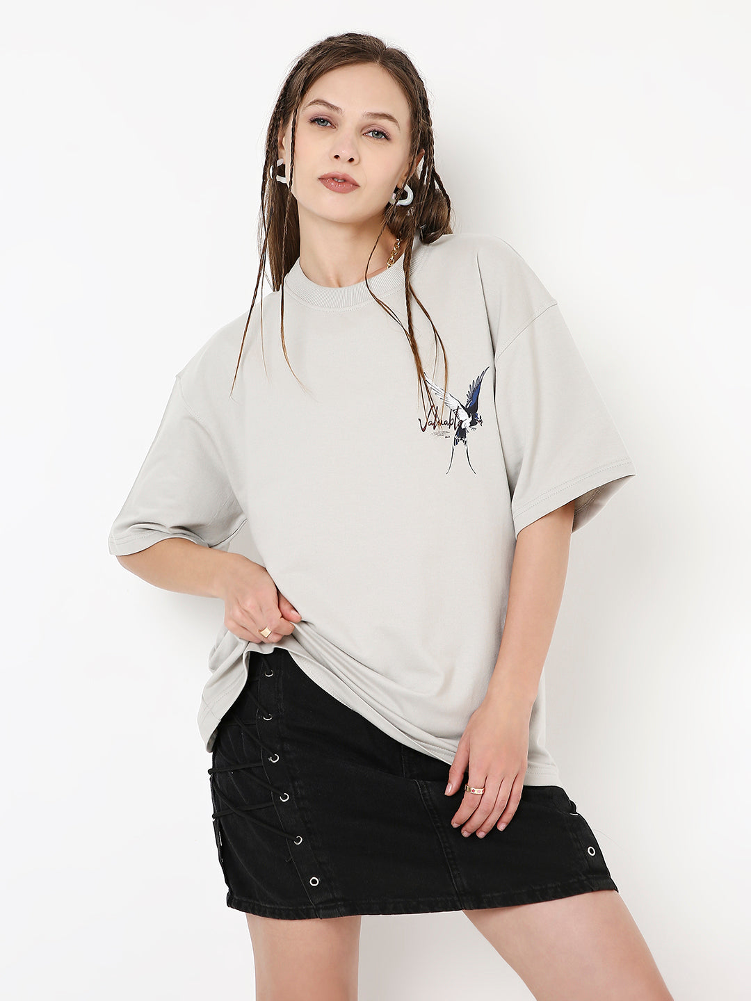 Oversized light beige T-shirt with abstract skipping stone print and short sleeves, worn with black buttoned skirt.