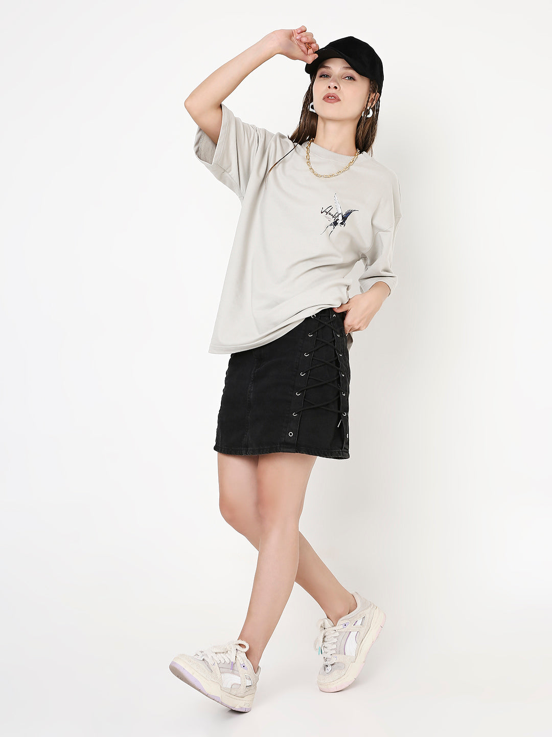 Oversize light gray T-shirt with small black skipping stone print, paired with black button-front skirt and white sneakers.