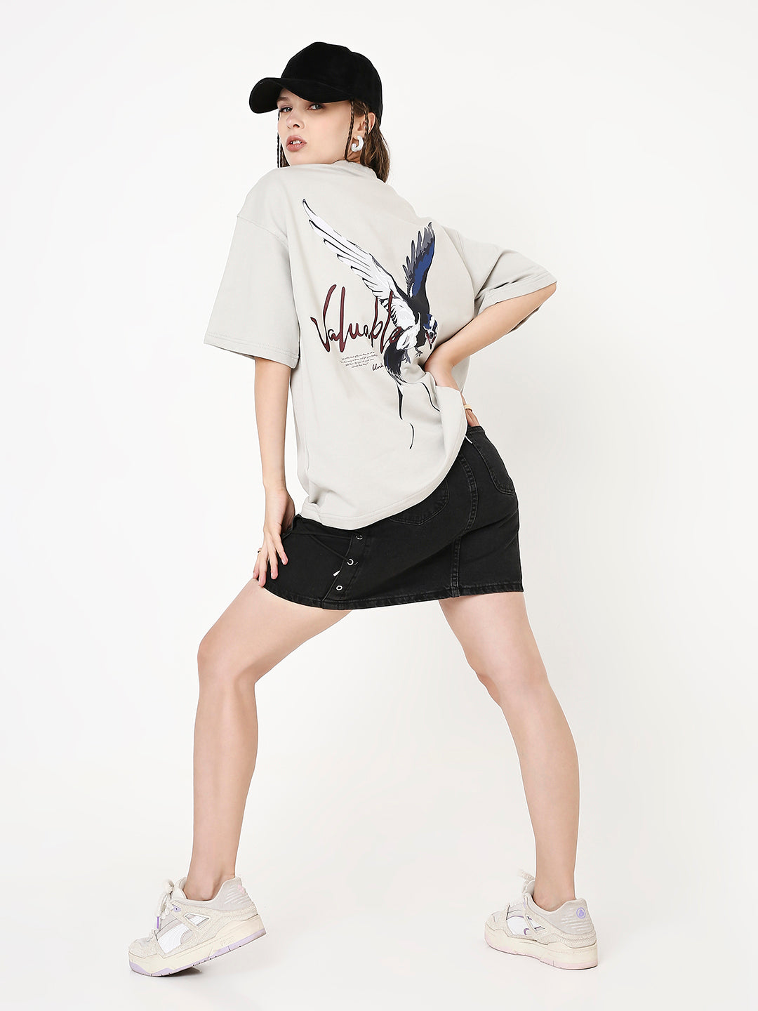 Oversize beige t-shirt with abstract skipping stone graphic and text on back, paired with black skirt and white sneakers.