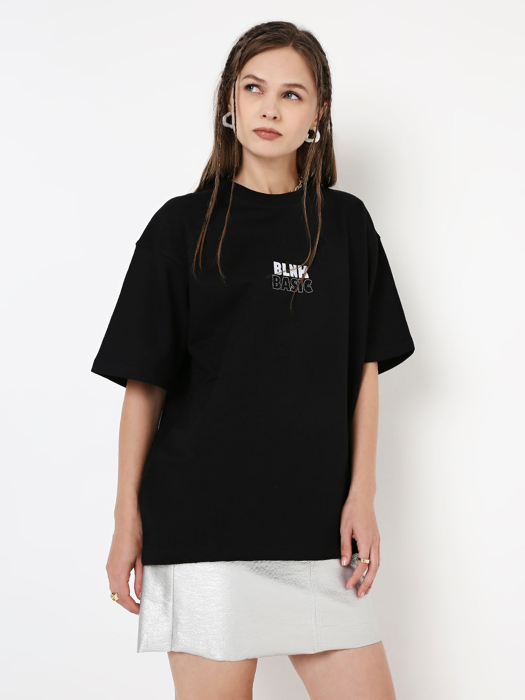 Oversize black T-shirt with small white and red text print on chest, worn with white skirt.