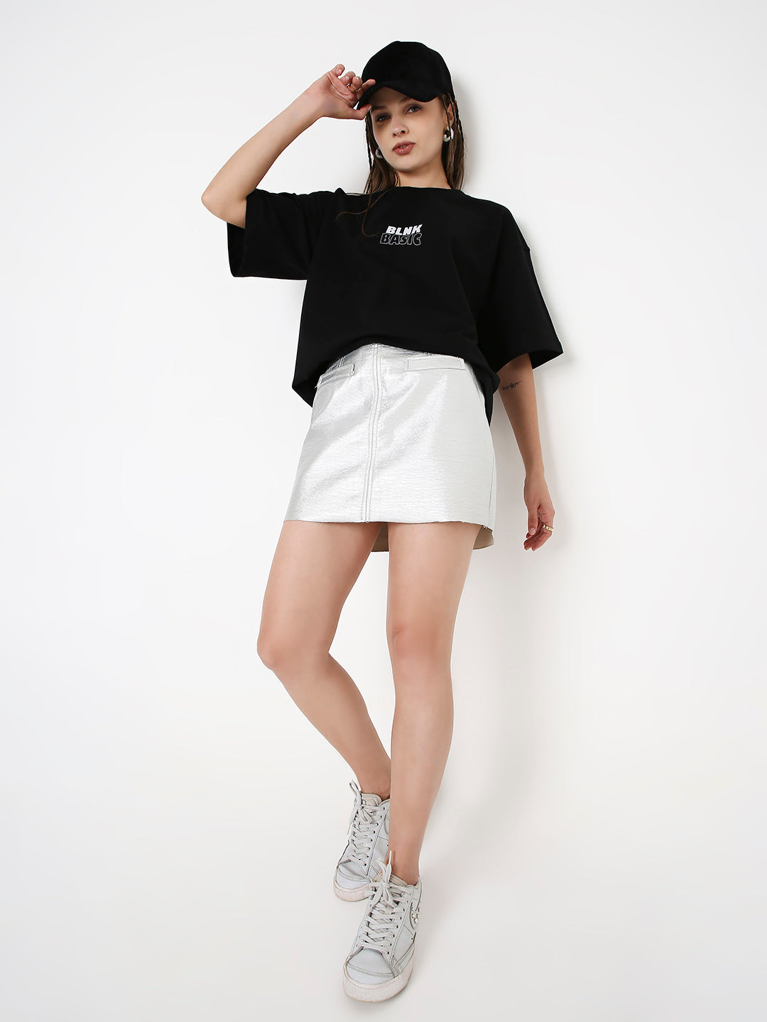 Oversize black T-shirt with white printed logo, paired with white mini skirt and sneakers.
