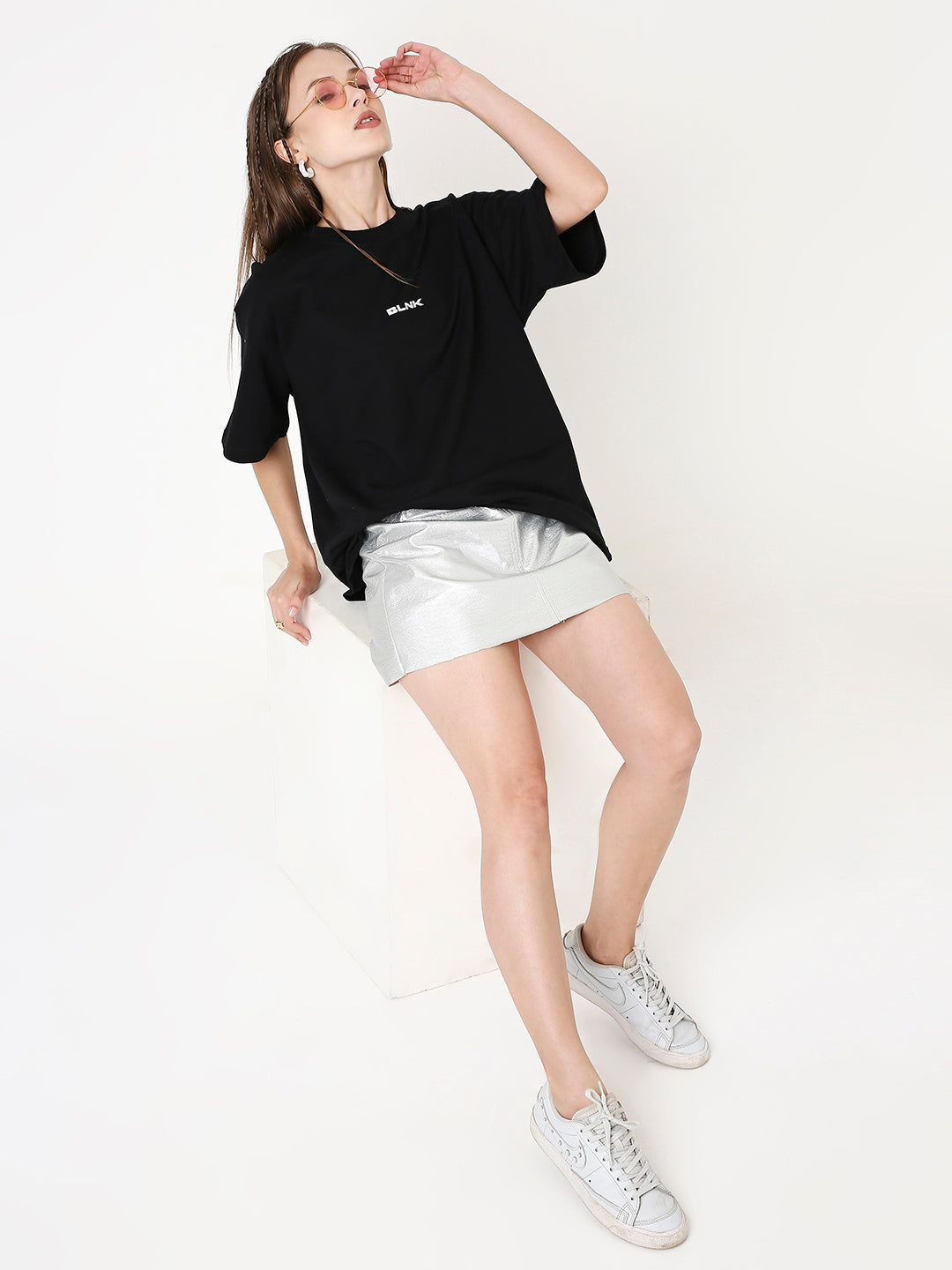 Oversize black T-shirt with small white front print paired with white mini skirt and sneakers.