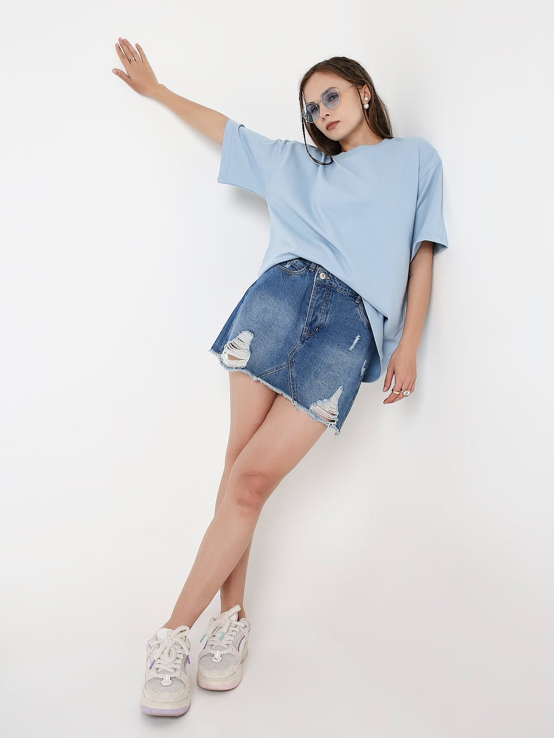 Oversize light blue solid t-shirt with short sleeves paired with distressed denim mini skirt and white sneakers.