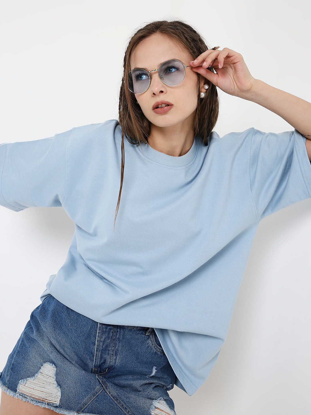 Oversize light blue solid t-shirt with dropped shoulders paired with distressed denim shorts and round blue sunglasses.