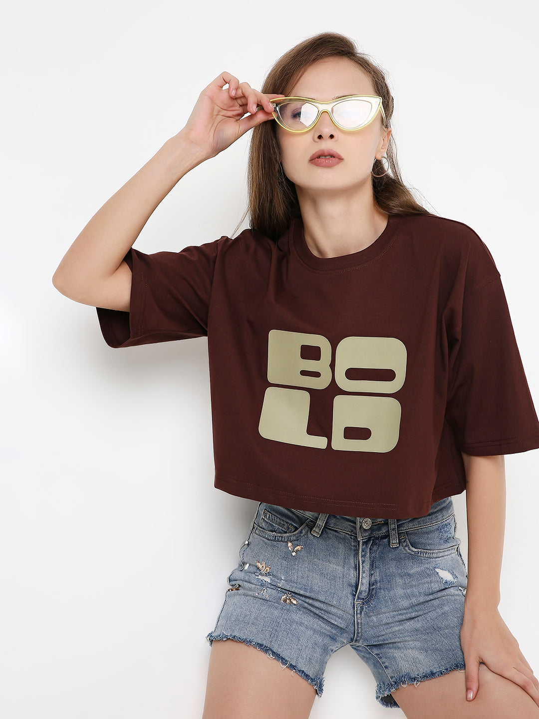 Brown oversized crop top with bold beige printed letters, paired with light denim shorts.