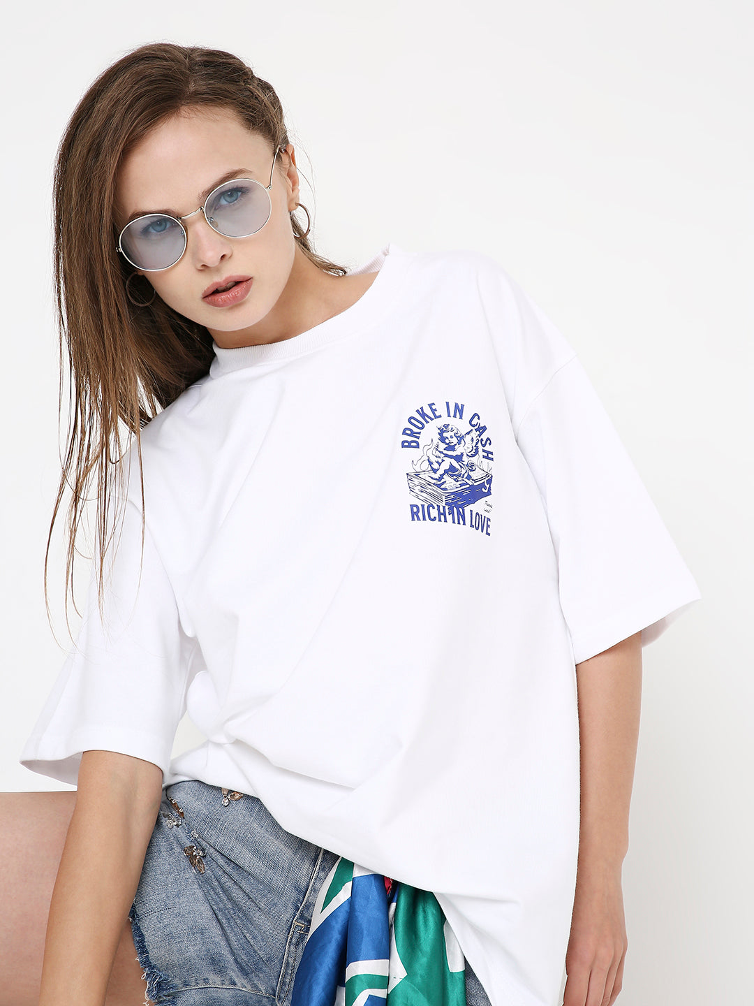 Oversize white T-shirt with blue graphic print on left chest, paired with sunglasses and casual jeans.
