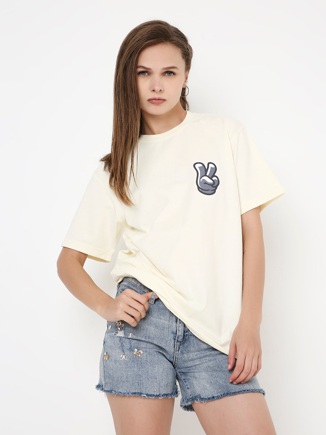 Off-white relaxed fit t-shirt with small navy peace sign print on left chest, paired with light blue denim shorts.
