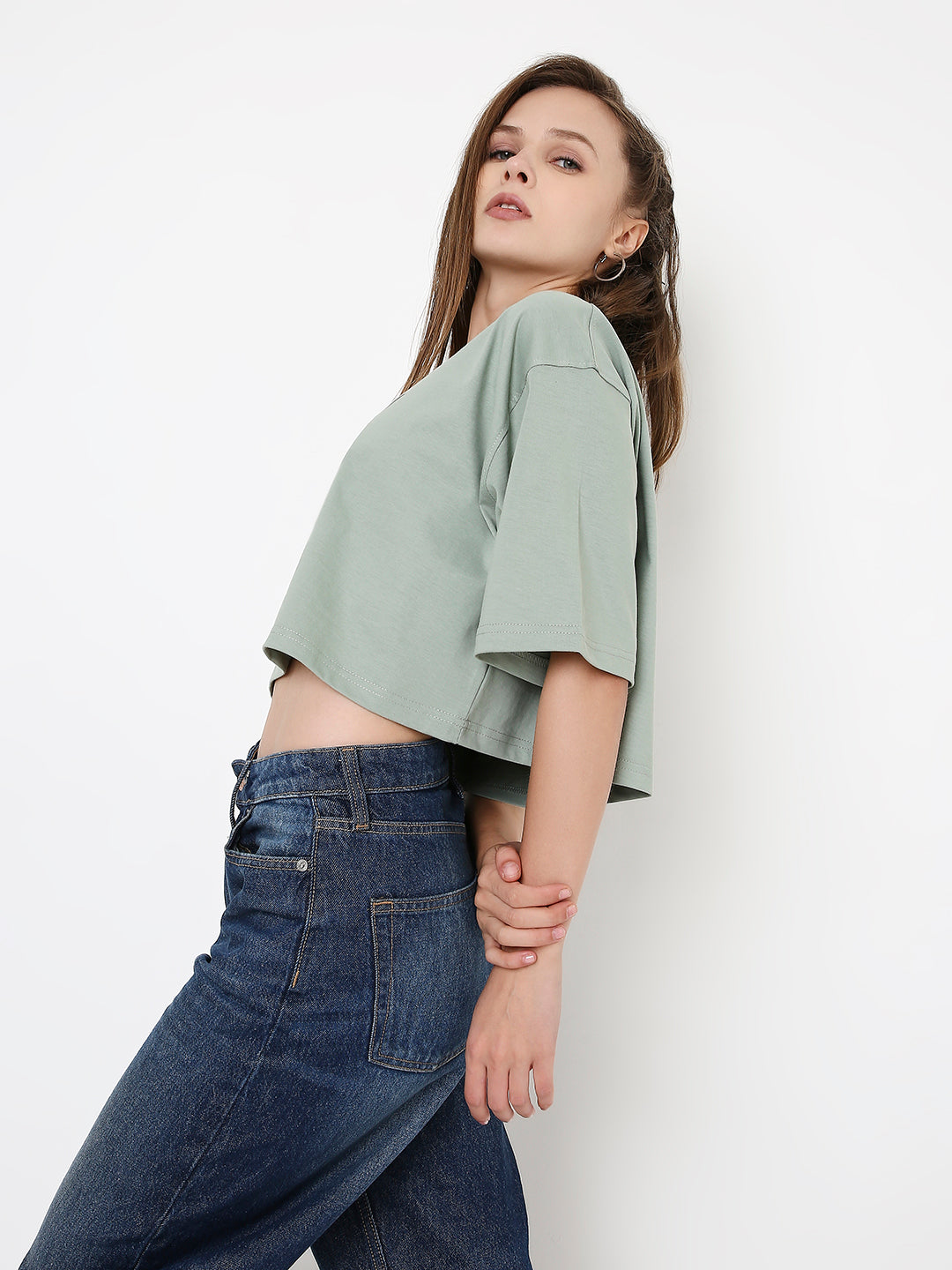 Oversize sage green crop top with elbow-length sleeves styled with high-rise dark blue jeans.