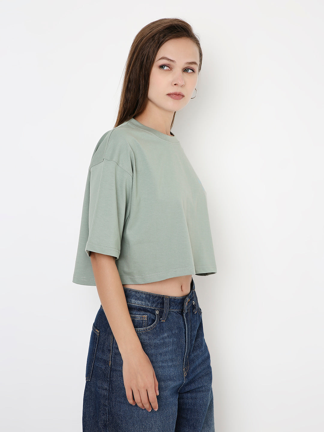Oversize sage green cropped top with loose sleeves paired with high-rise blue jeans.