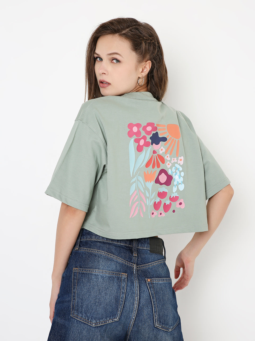 Sage green oversized crop top with pink and orange floral graphic on back, paired with blue denim jeans.