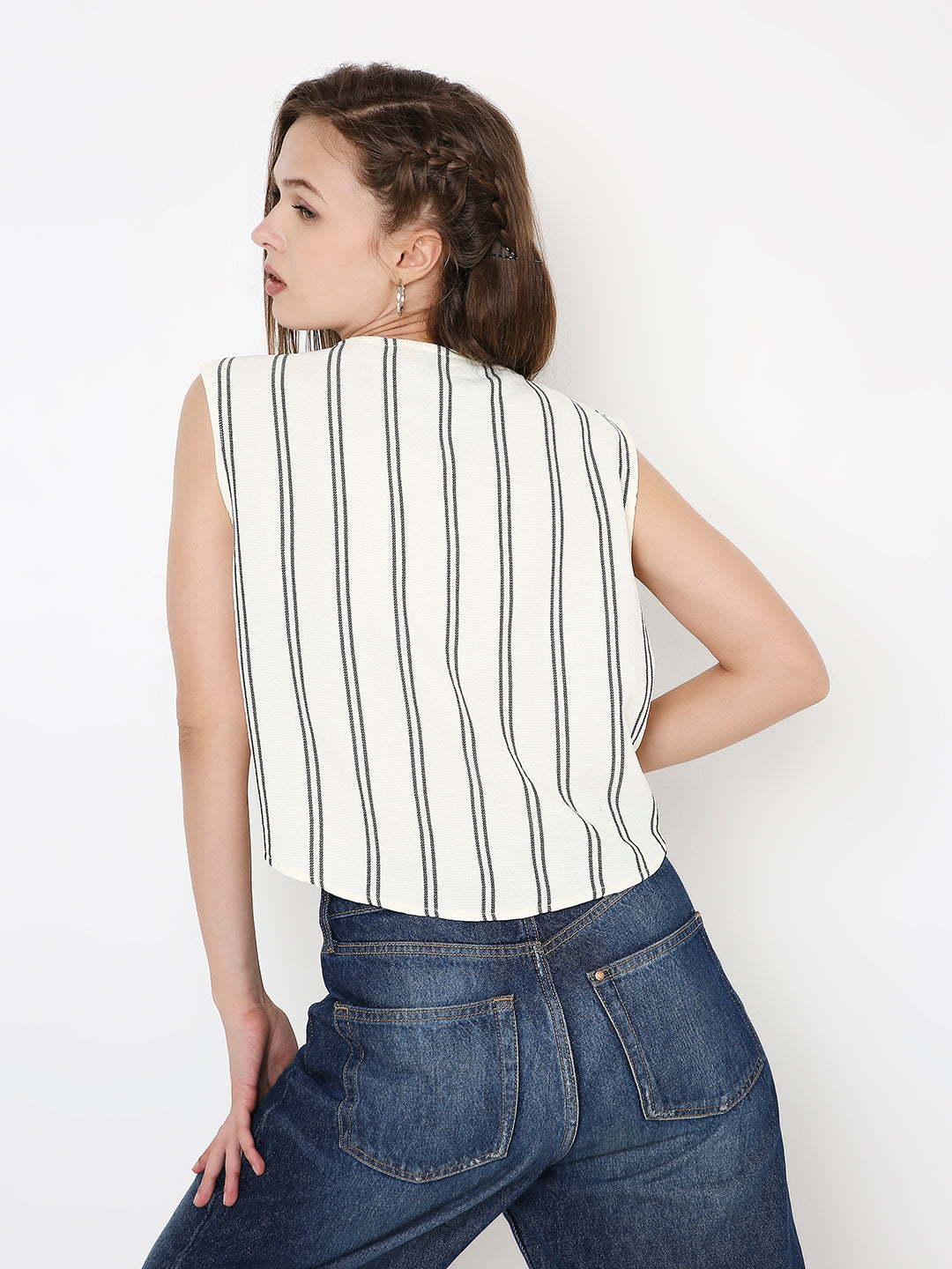 White crop top with vertical black stripes and sleeveless design worn with blue jeans, shown from back.