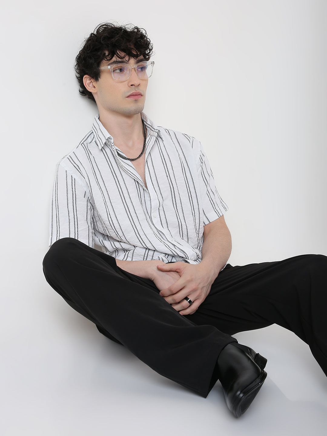 Person wearing a striped shirt and black pants sitting on a white background