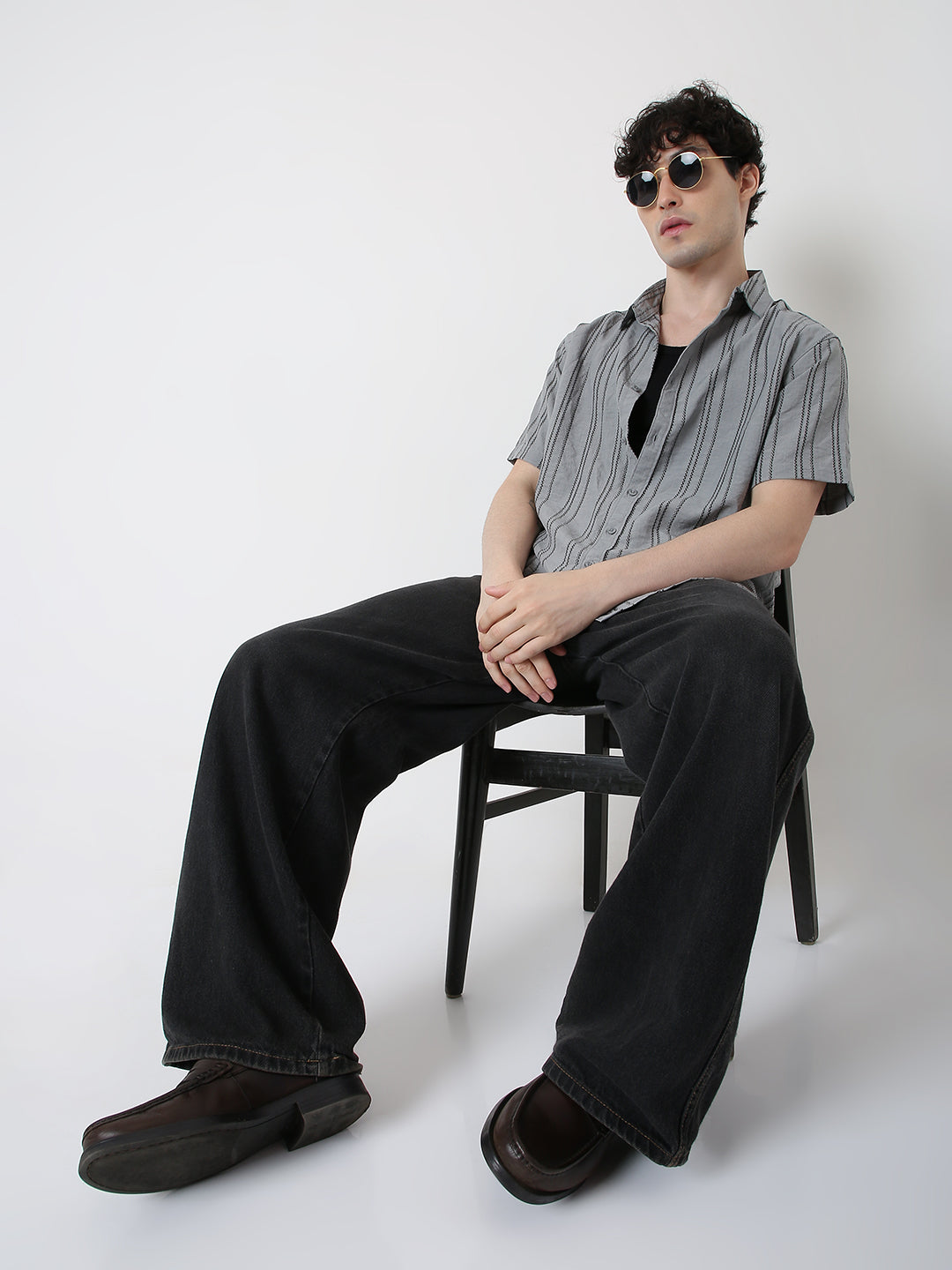 Man sitting on a chair wearing a striped shirt and sunglasses against a white background