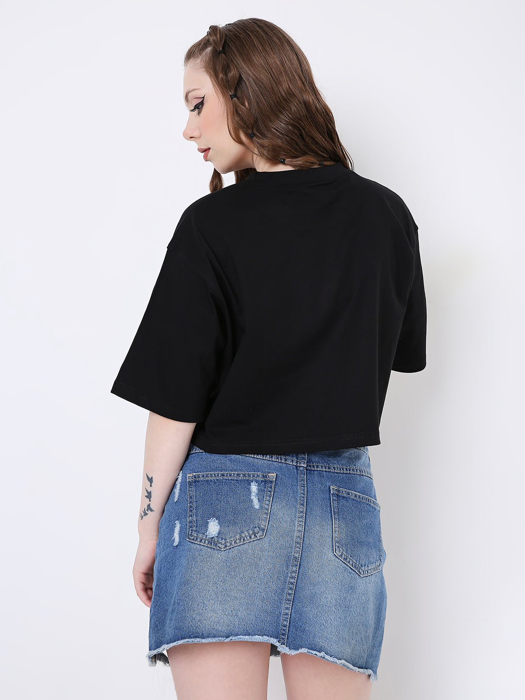 Black oversized crop top with short sleeves, worn with a distressed blue denim mini skirt.