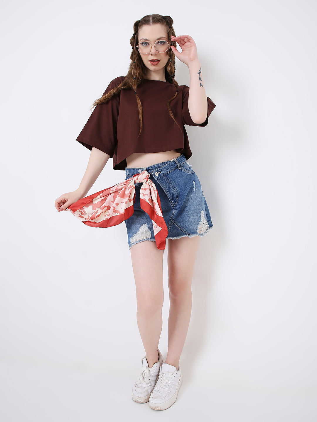 Oversize brown crop top with short sleeves paired with distressed denim shorts and a red patterned scarf belt.