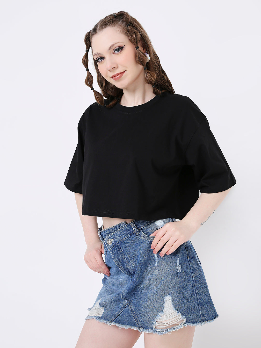 Black oversized crop top with short sleeves and a crew neckline worn with distressed denim skirt.