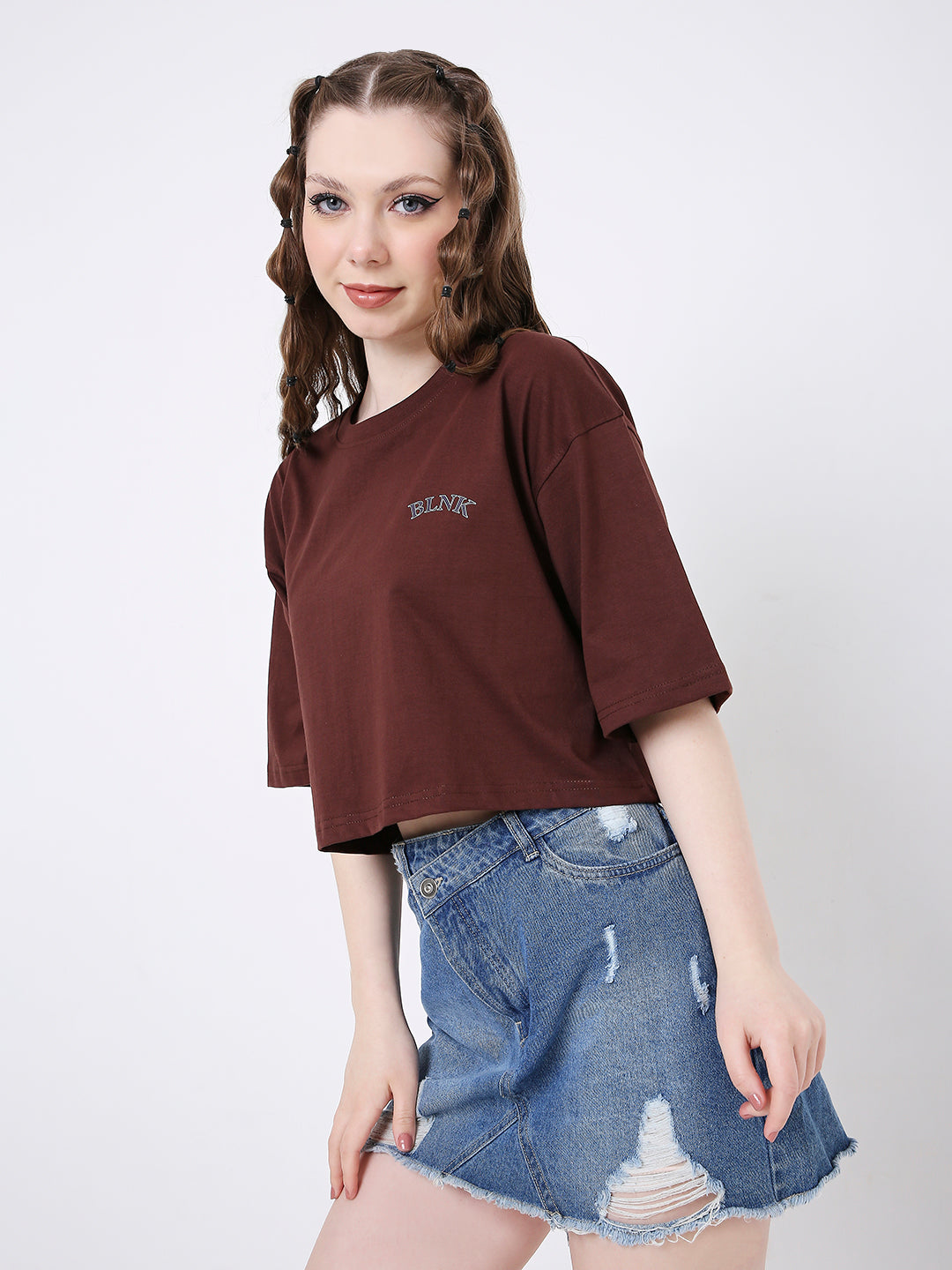 Oversize brown cropped T-shirt with short sleeves and small chest print paired with distressed denim skirt.