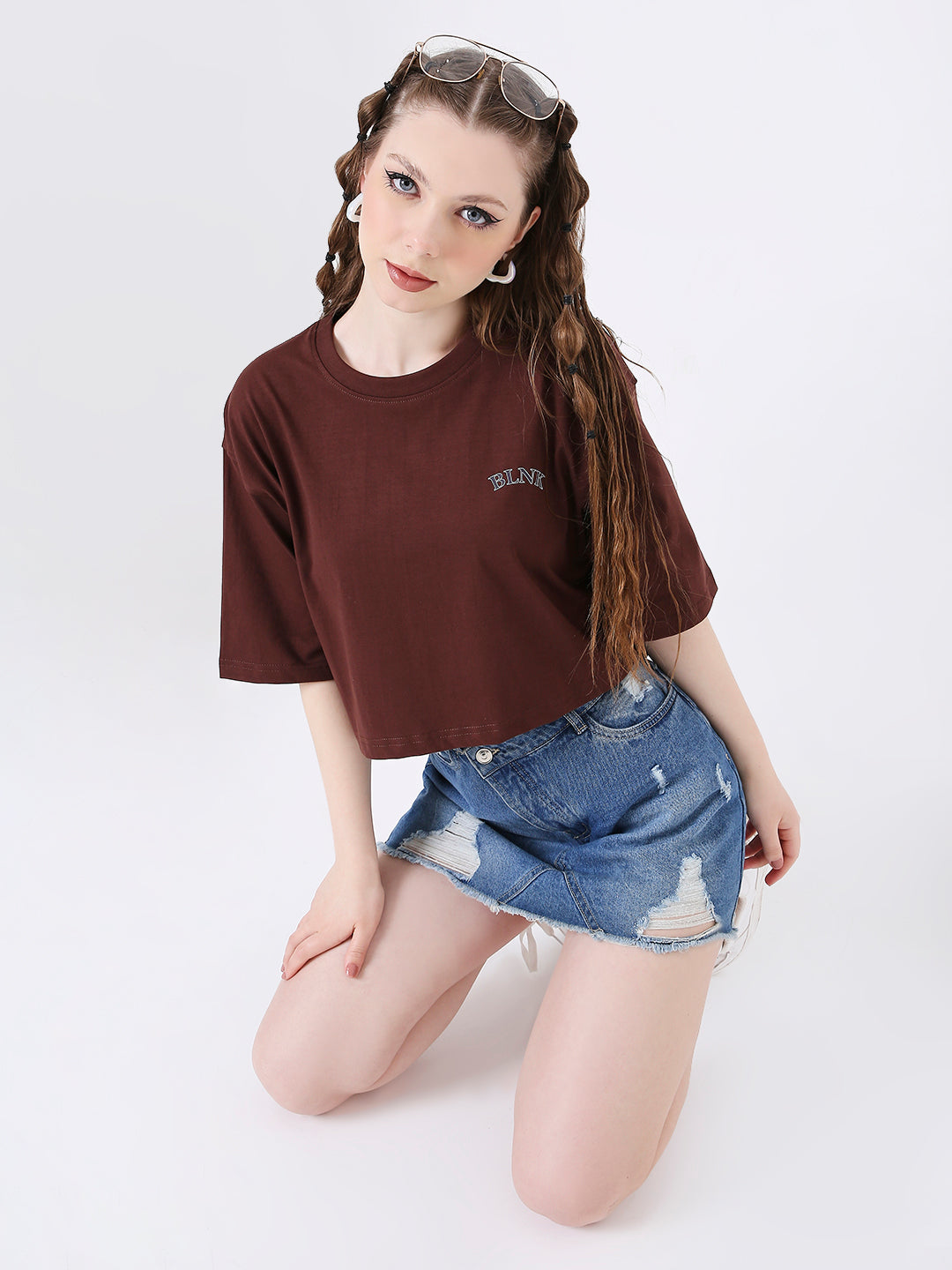 Oversize brown crop top with short sleeves and small white logo on chest, paired with denim skirt.