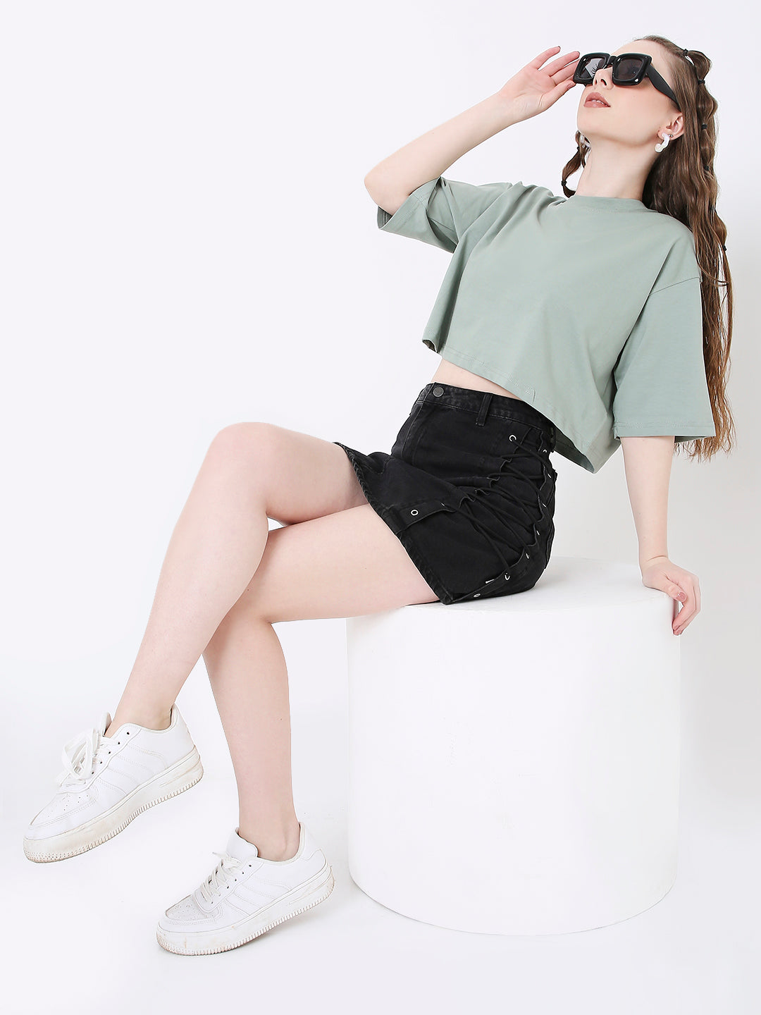 Oversize sage green crop top with short sleeves and crew neckline paired with black denim shorts.