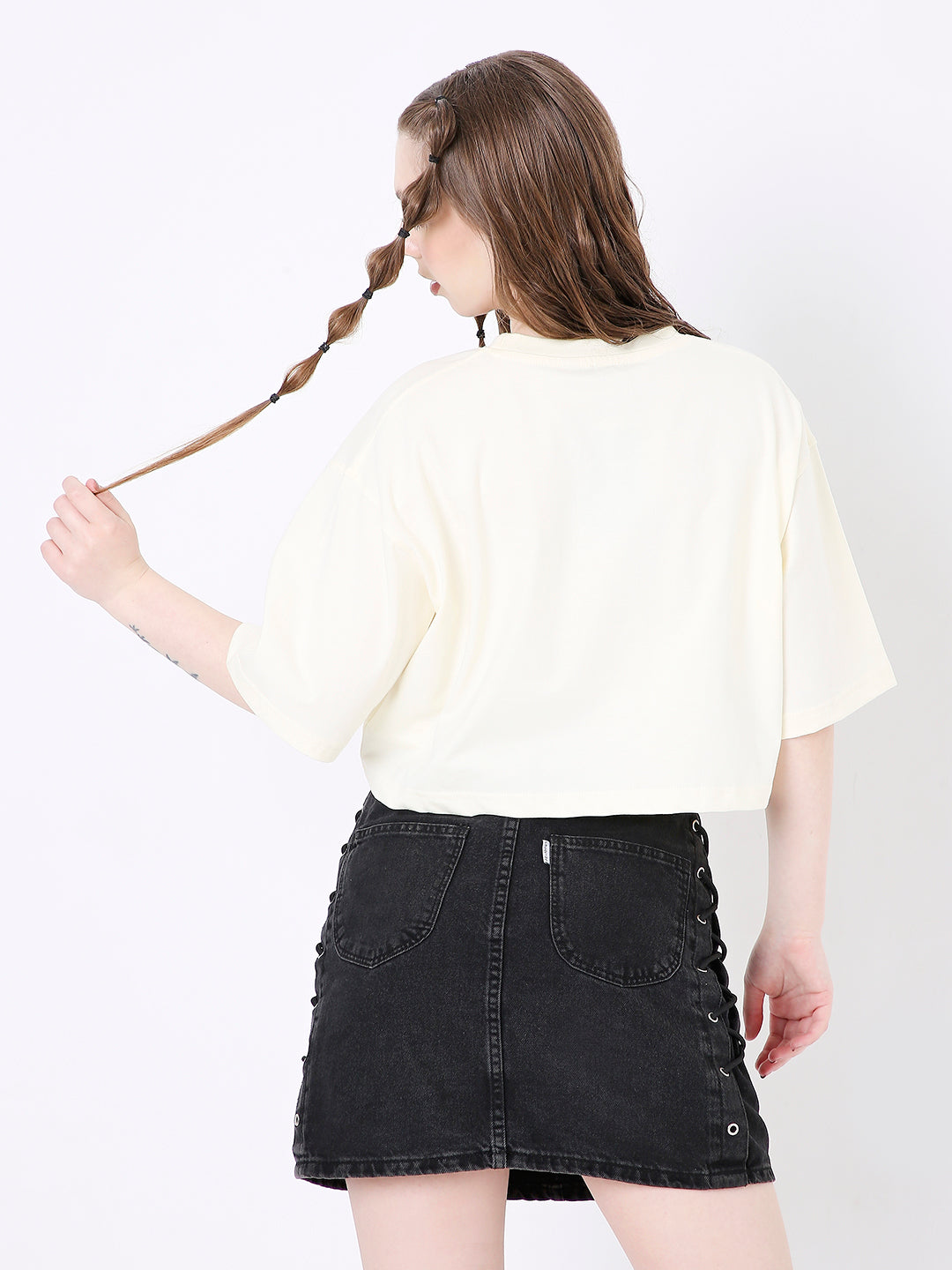 Off-white oversized crop top with short sleeves paired with a black distressed denim mini skirt.