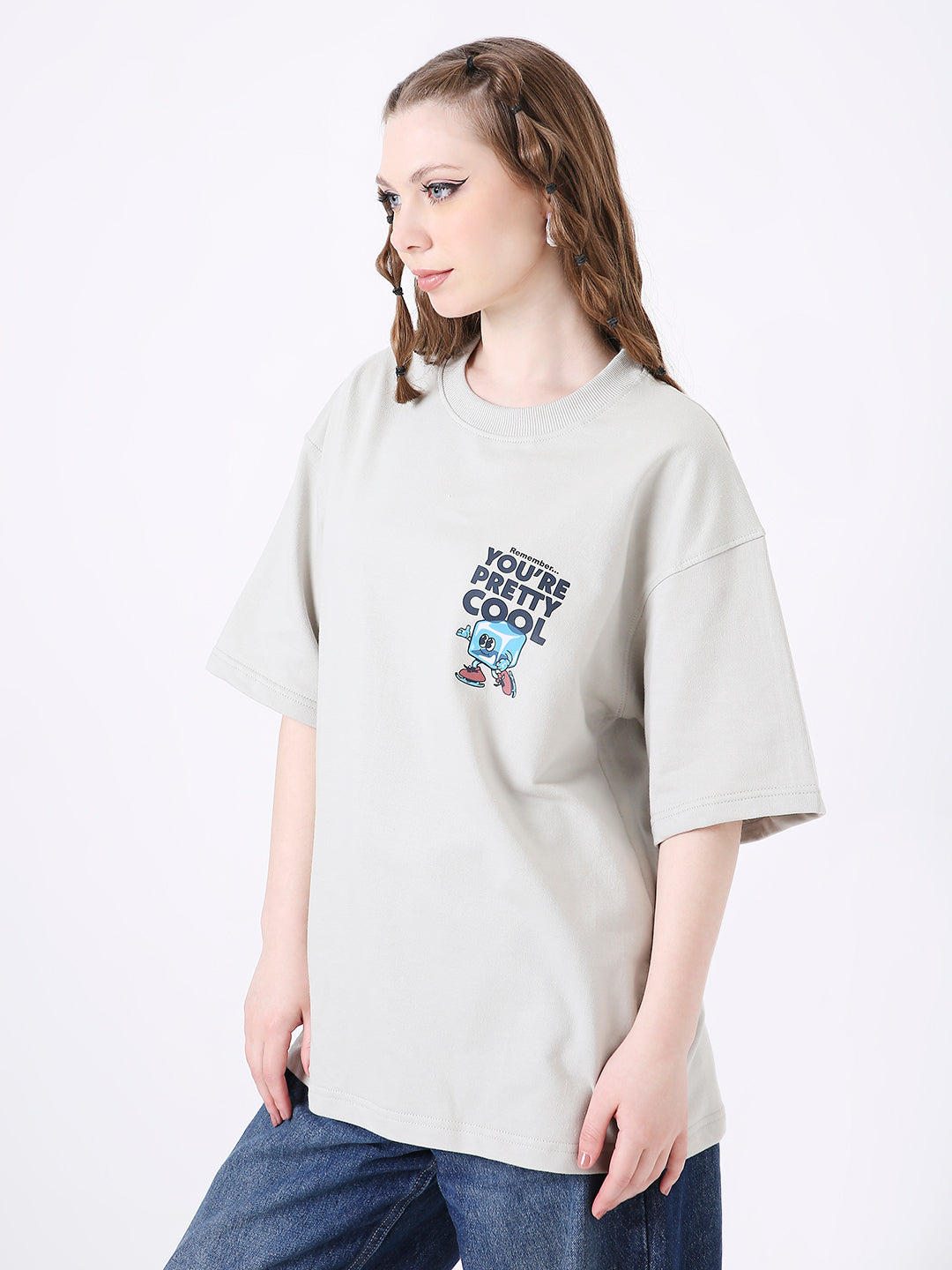 Light gray oversized T-shirt with small colorful skipping stone graphic and text on chest, worn with blue jeans.