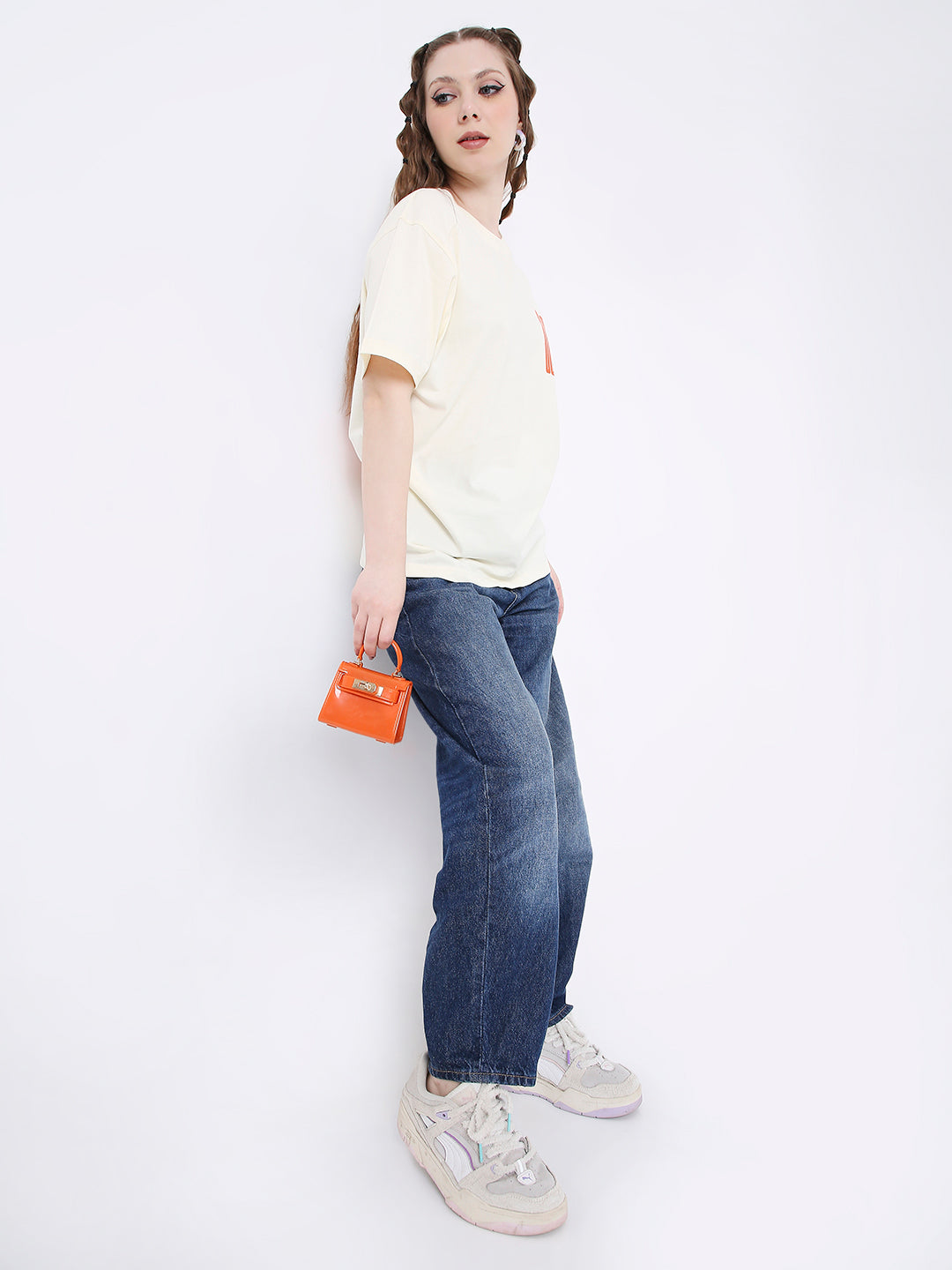 Off-white relaxed fit printed t-shirt paired with blue jeans and white sneakers, small orange handbag accessory.