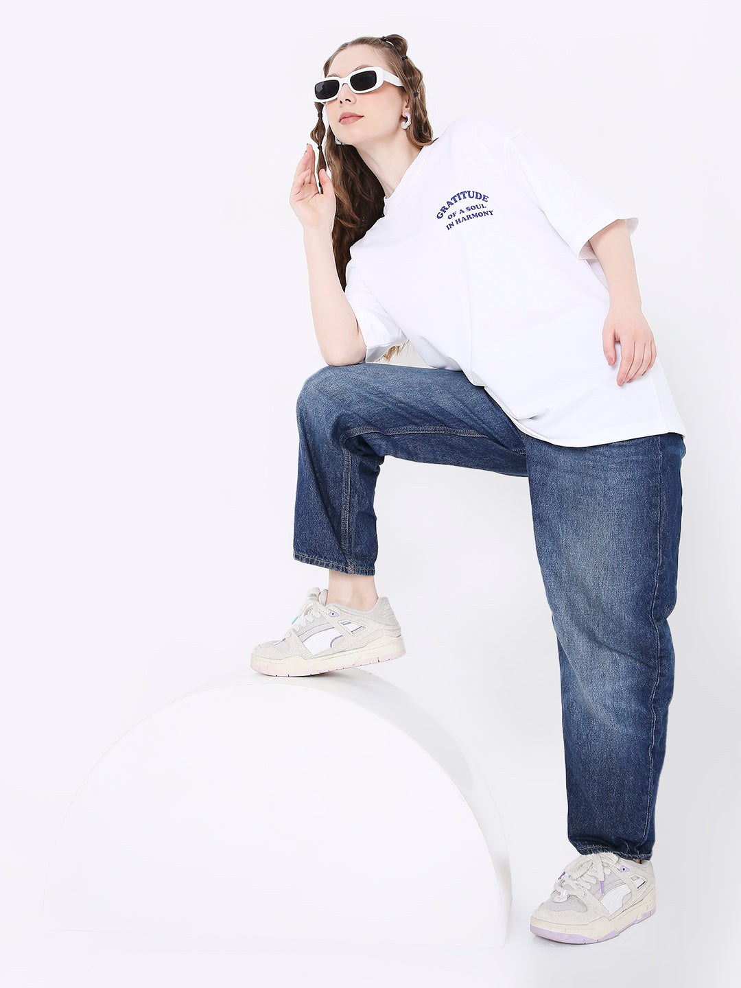 Oversize white T-shirt with small navy print on chest, paired with blue jeans and white sneakers.