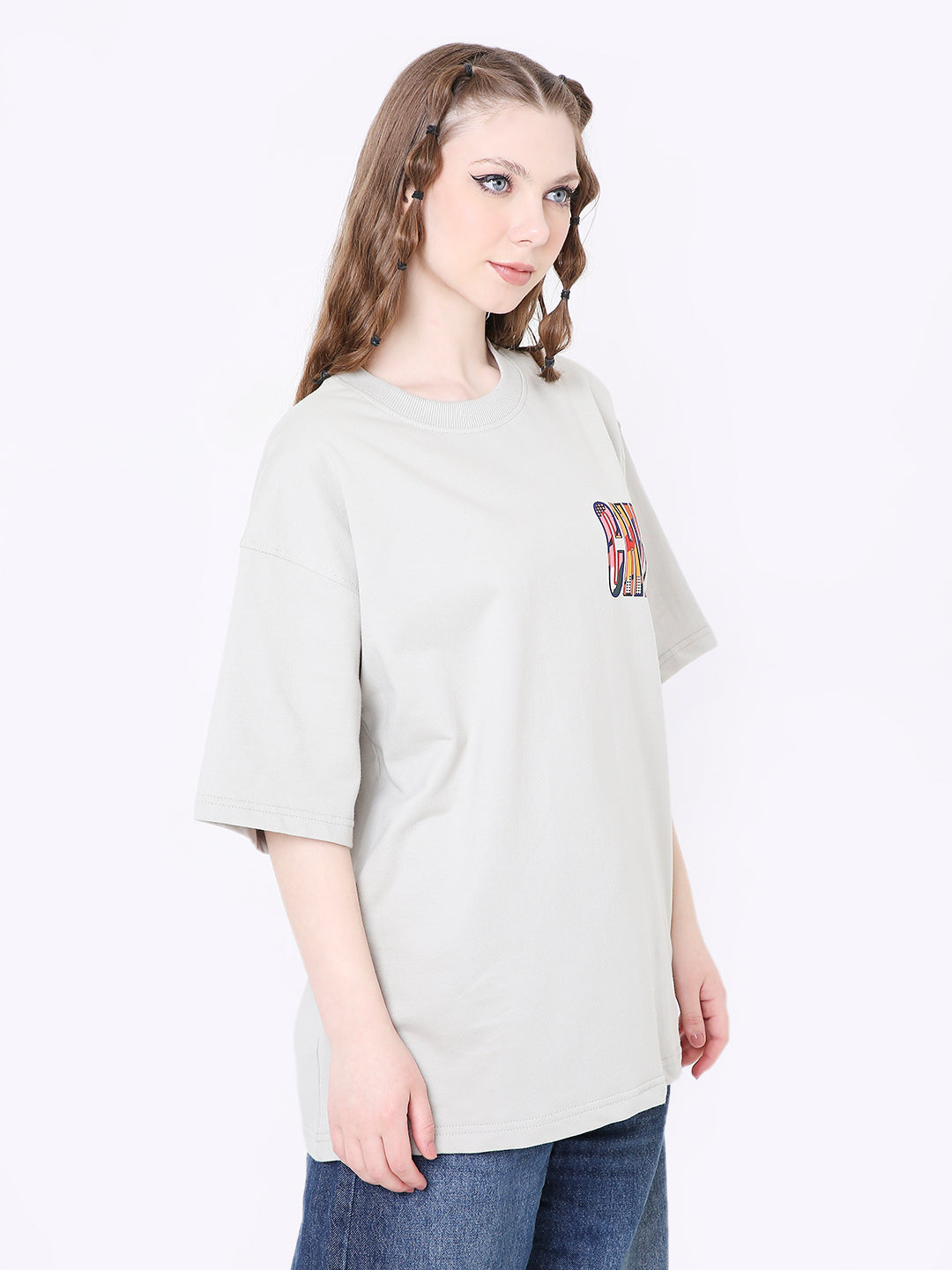 Light gray oversized T-shirt with small colorful skipping stone print on left chest, paired with blue jeans.