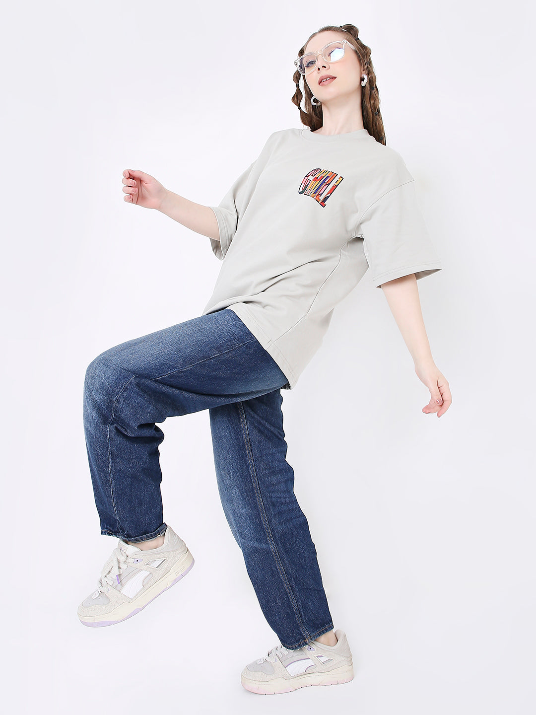 Light gray oversized t-shirt with colorful skipping stone print on chest, paired with blue jeans and white sneakers.