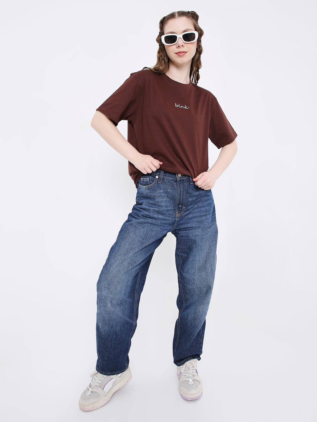 Relaxed fit brown printed t-shirt with small white text logo, paired with blue jeans and white sneakers.