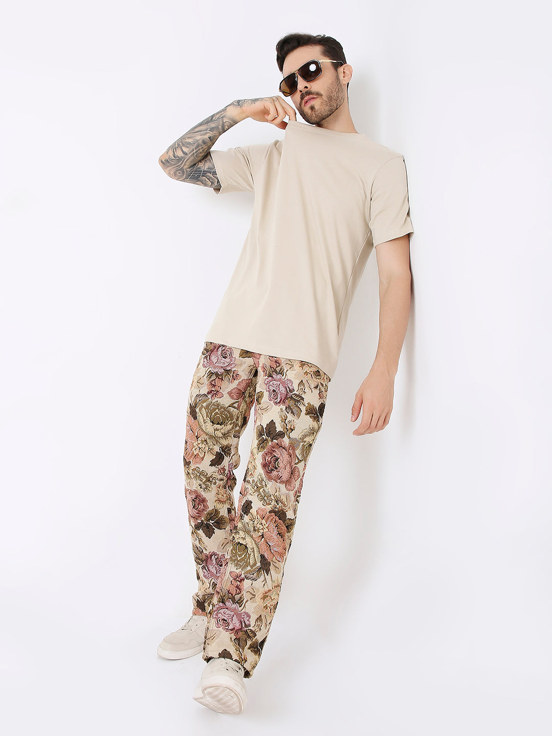 Man wearing a relaxed fit sand-colored t-shirt with floral patterned pants and white sneakers.