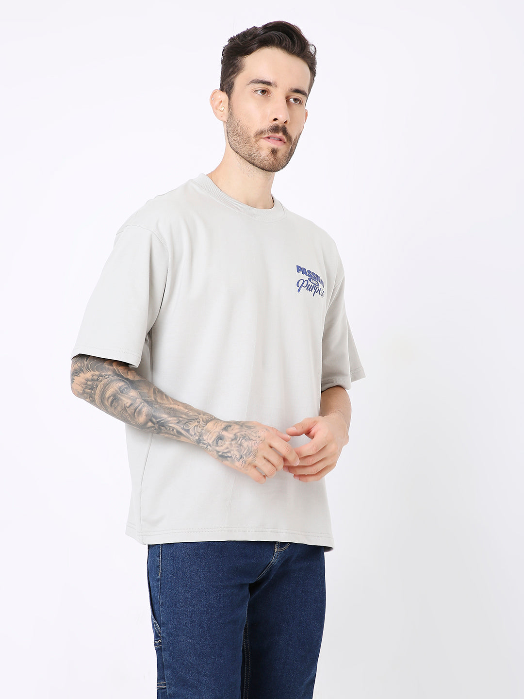 Light gray oversized t-shirt with small dark blue skipping stone graphic on left chest, worn with dark blue jeans.