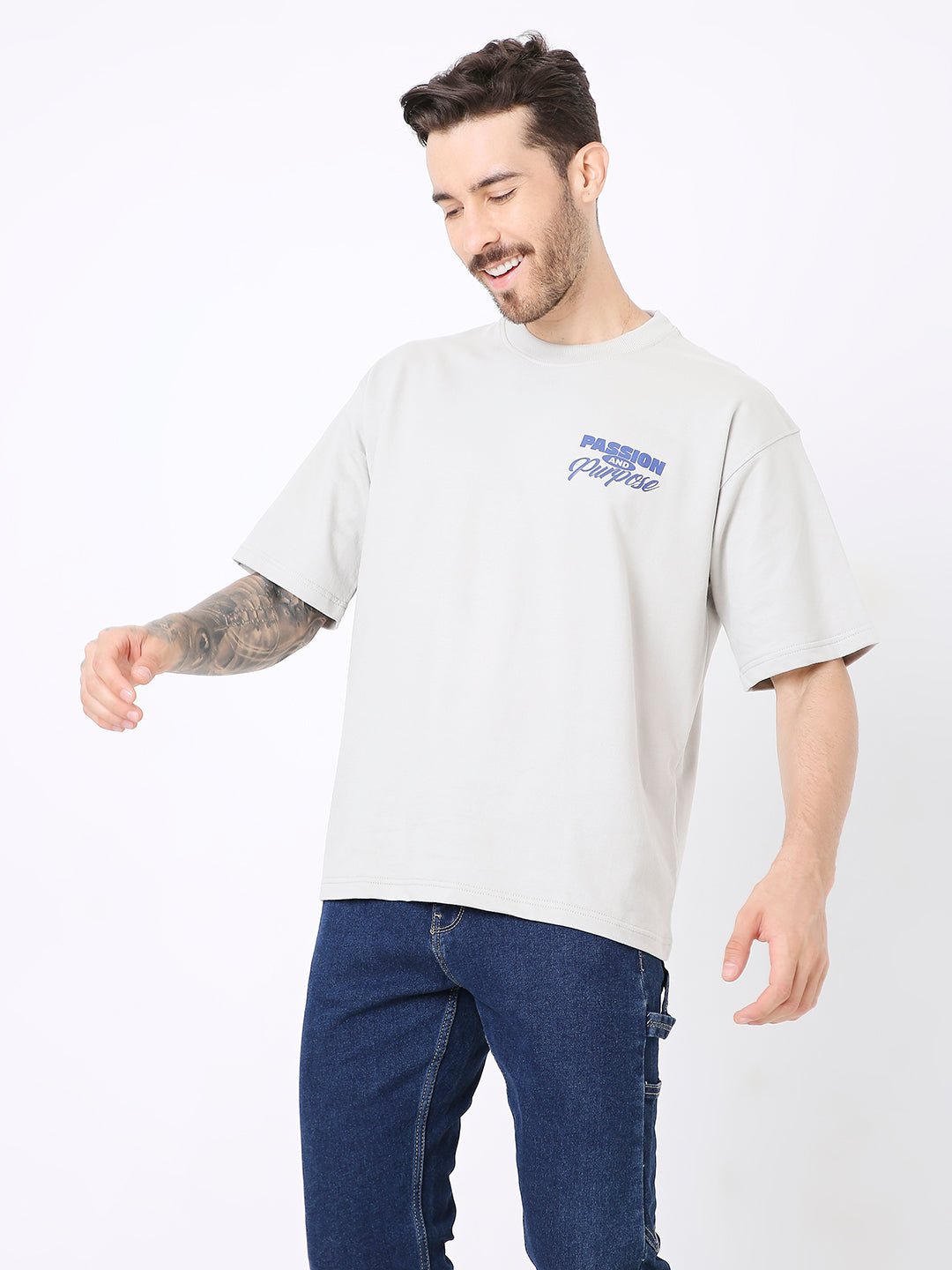 Light gray oversized t-shirt with small blue skipping stone graphic on left chest, paired with dark blue jeans.