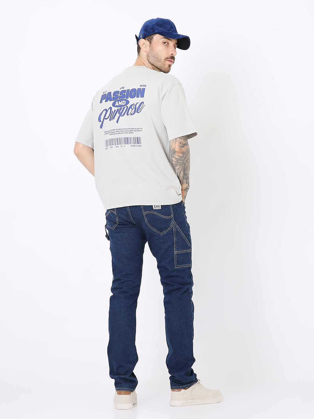 Off-white oversized t-shirt with royal blue skipping stone graphic on back, paired with dark blue jeans and navy cap.