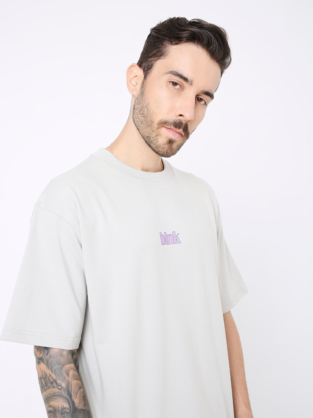 Light gray oversized t-shirt with small purple skipping stone graphic on chest and dropped shoulders.
