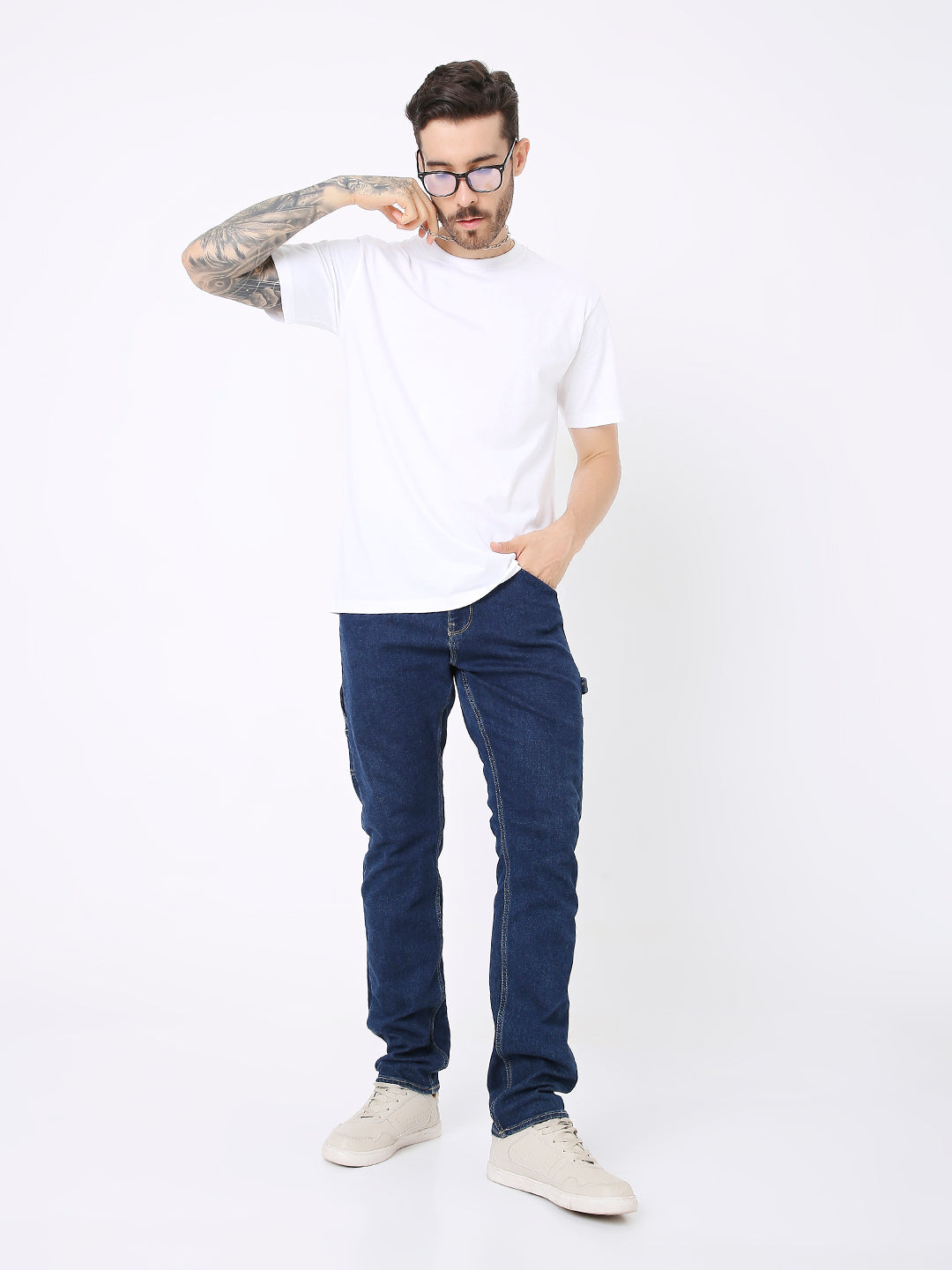 Man wearing relaxed-fit white solid t-shirt with navy blue jeans and beige sneakers.