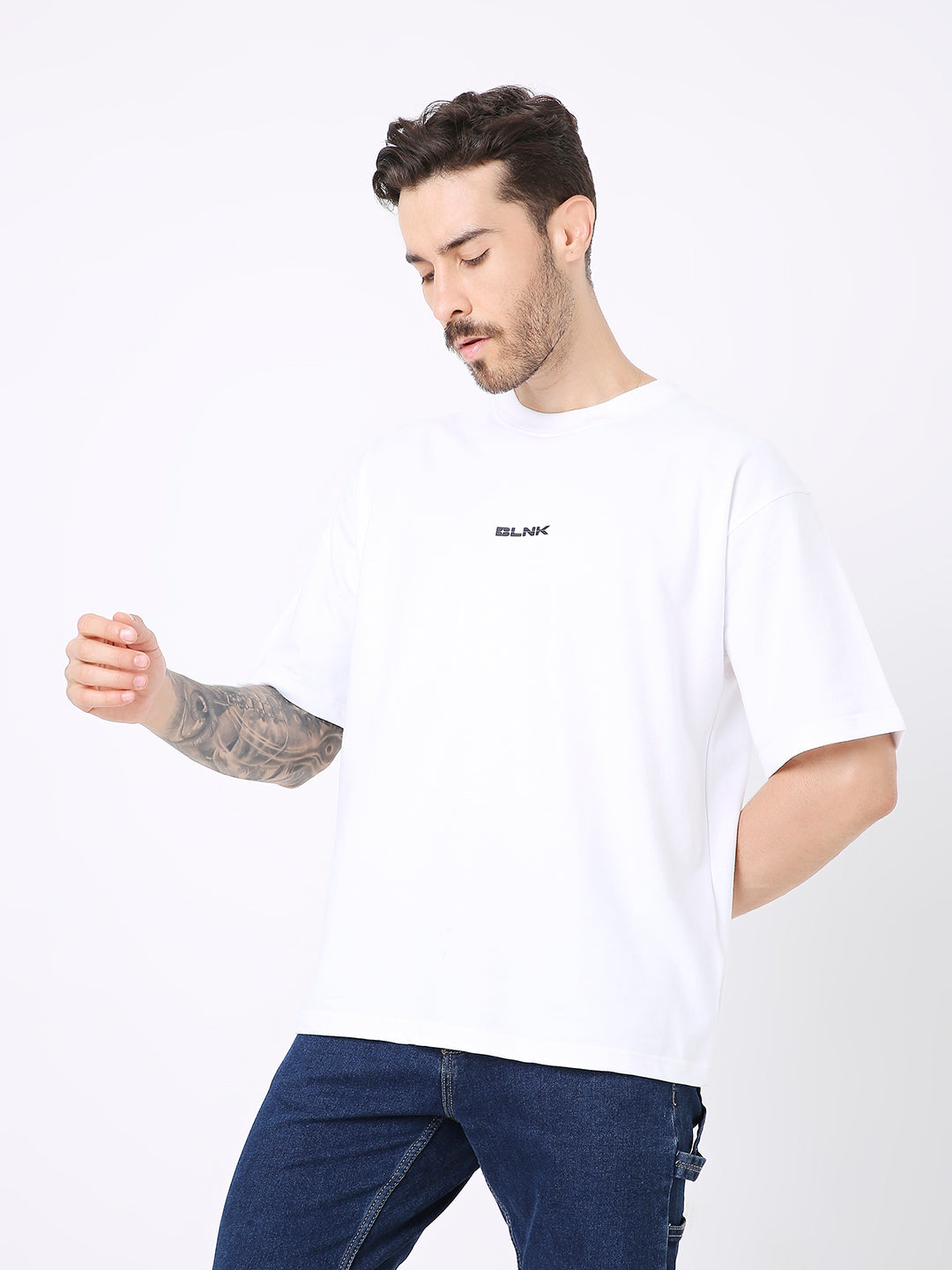 Oversize white t-shirt with small black logo print on chest, worn with dark jeans.
