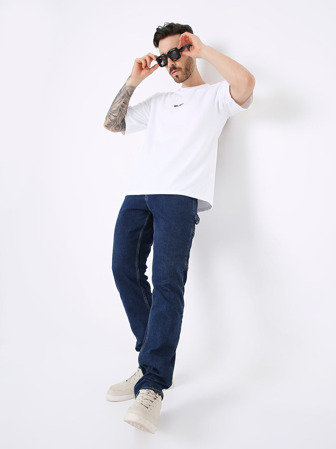 Oversize white t-shirt with small black print on chest, paired with dark blue jeans and beige sneakers.