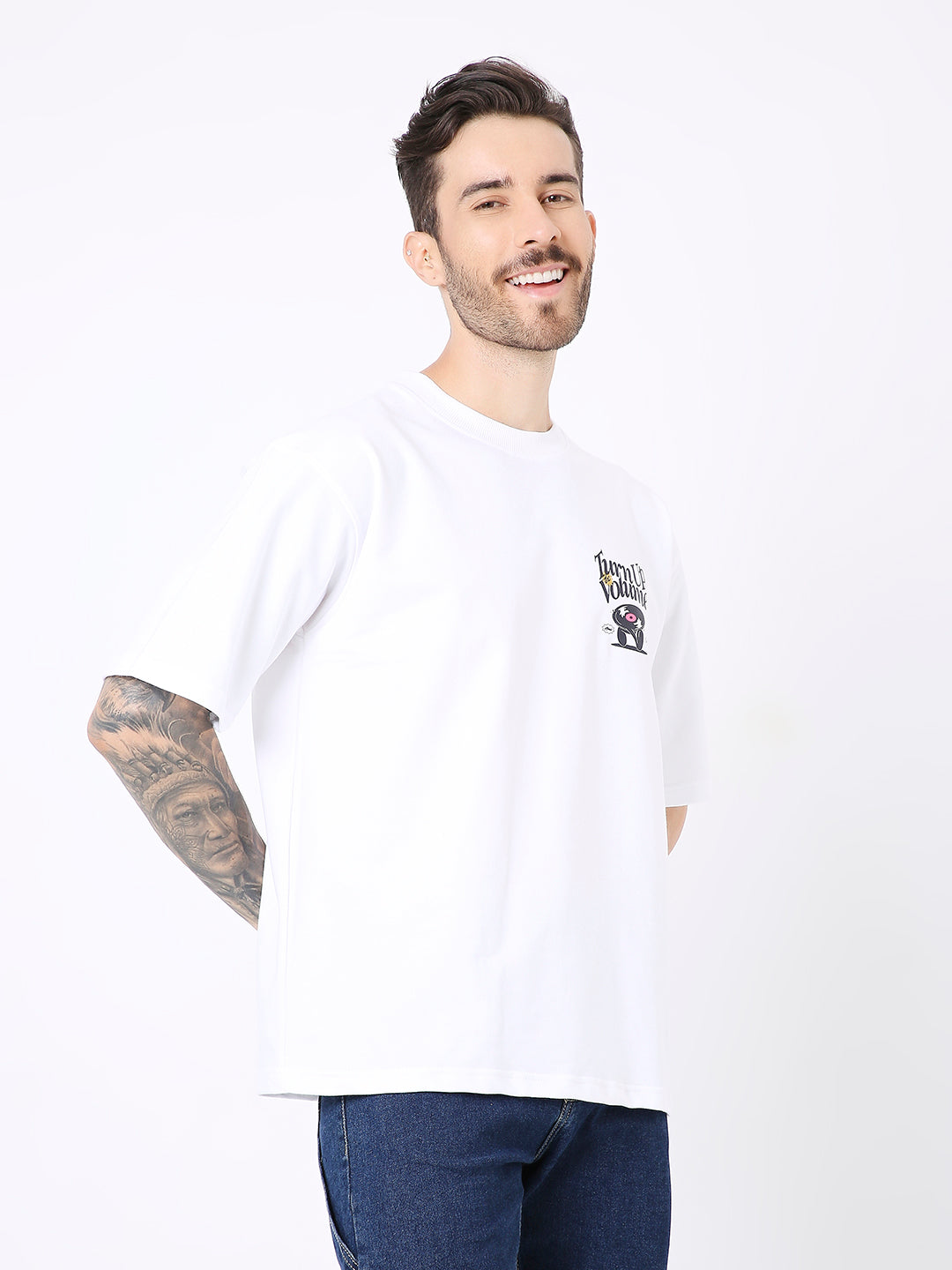 Oversize white T-shirt with small colorful graphic on left chest, styled with dark jeans.