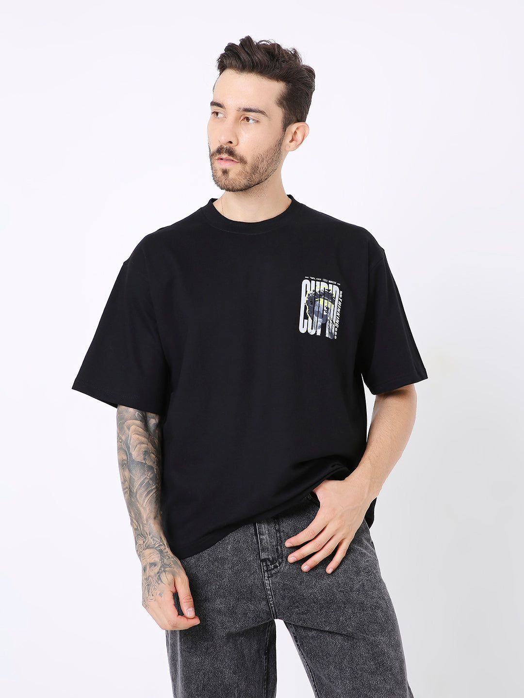 Oversize black t-shirt with small white and gray rectangular print on chest, worn with dark gray jeans.
