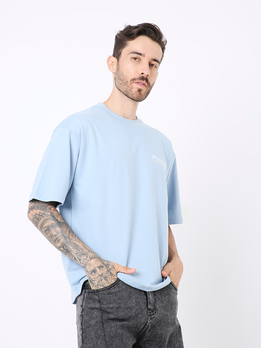 Light blue oversized t-shirt with subtle chest print, worn with black jeans.