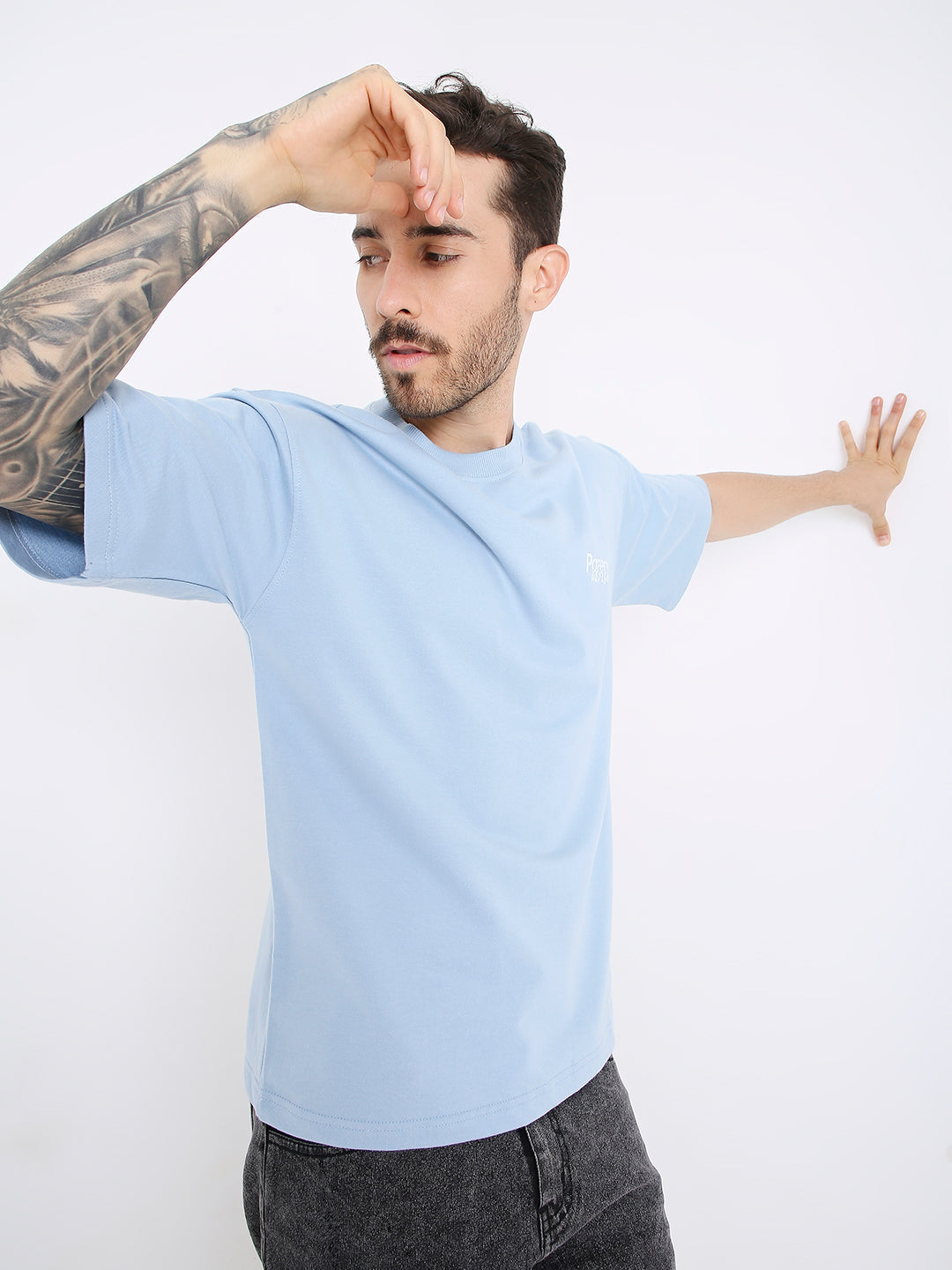 Light blue oversized T-shirt with subtle printed text worn by tattooed man.